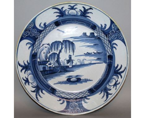 A DELFTWARE CIRCULAR CHARGER, LONDON, CIRCA 1760, painted with under-glaze blue, woman beneath a tree, two boats, mountain an