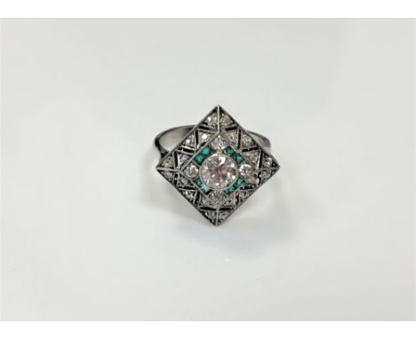 A white gold Art Deco style emerald and diamond ring, the square setting with grain set brilliant cut centre stone surrounded