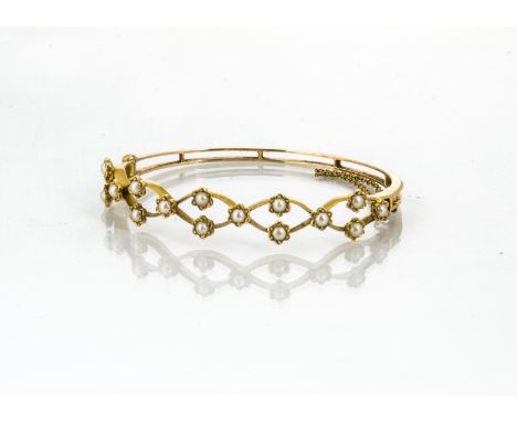 An Edwardian yellow metal and seed pearl bangle, the oval pierced design set with stylised flowers centred with seed pearls o