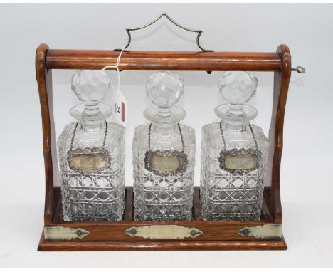 An oak cased three decanter tantalus, w.34cm, each decanter bearing a silver label, inscribed for Whisky, Brandy and GinTanta