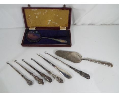 A good lot to include six silver handles button hooks (varying assays), a white metal serving slice and plated serving spoon 