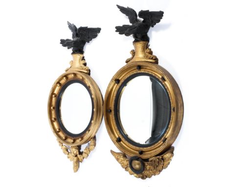 Two Regency giltwood hall convex mirrors, each surmounted with a black painted gesso eagle finial suspending a ball on gilt p