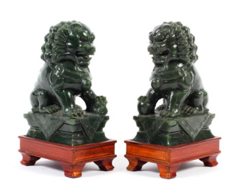 A pair of Chinese carved spinach green jade lion dogs seated on a pedestal, 20th century, height 14cm, on carved wood stands