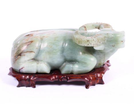 A Chinese carved jade model of a water buffalo on wooden stand, 20th century, modelled recumbent, celadon colour with brown s