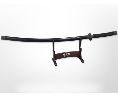 A 20th-century Japanese katana in lacquered scabbard on wooden sword stand, overall length 113cm.