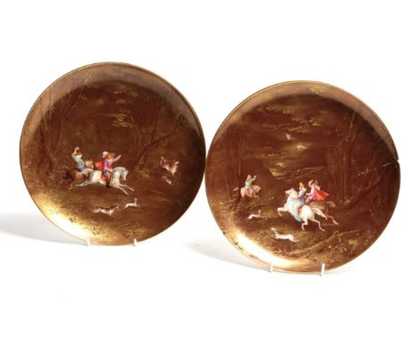 A pair of 19th century Limoges plates painted with hunting figures on horseback on a monochrome gilt background 
