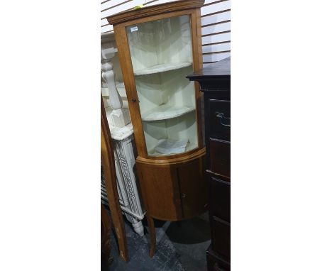 A 20th century light oak corner cabinet, the bowfront glazed door enclosing shelves, above two cupboard doors under, to splay