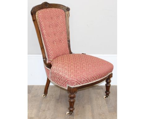 A Victorian low or nursing chair with patterned red upholstery, carved exposed mahogany frame and brass and ceramic castors, 