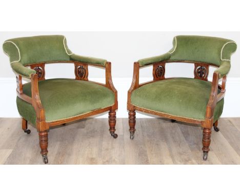 A pair of Victorian low arm or tub chairs with exposed and carved mahogany frame, green upholstery, turned legs and brass and