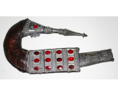 A Middle Eastern jambiya type dagger, white metal mounted eather scabbard set with red paste, length 33cm.