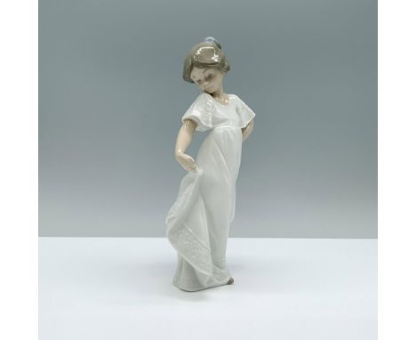 A figurine of a young girl, dressed in white, as she playfully lifts the end of her dress to steal a glance. Nao by Lladro ba