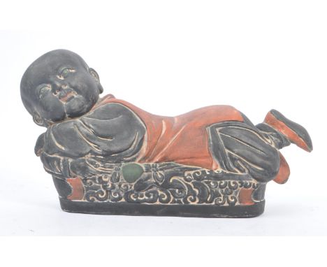An early 20th Century Chinese ceramic / clay pillow in the form of a lounging Buddha like / baby figure laying forwards upon 