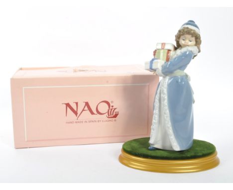 Nao by Lladro - A 20th Century china porcelain Nao by Lladro ' Christmas Time ' figurine of girl in long coat and hat carryin