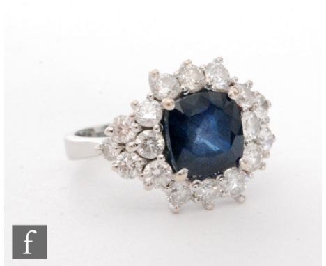 An 18ct white gold sapphire and diamond cluster ring, central cushioned square sapphire, length 9mm, within a border of twelv