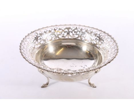 An antique silver fruit basket of circular bowl form with pierced scroll and fleur de lis rim raised on three scroll feet wit