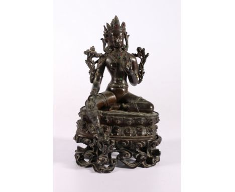 A 19th century Indian bronze Tara seated on a double lotus throne, with inset glass 'jewels', carved and pierced wooden wave 