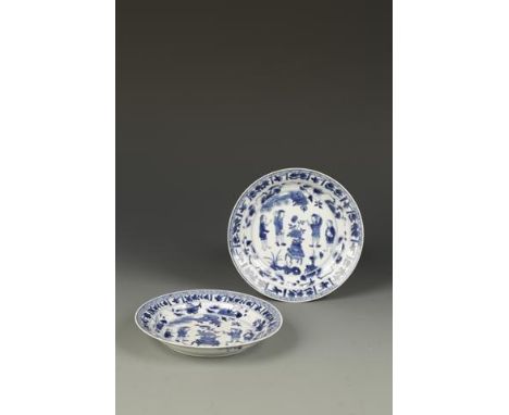 A PAIR OF CHINESE BLUE AND WHITE SAUCER DISHES showing Dutch traders standing around a central vase of flowers, within foliat