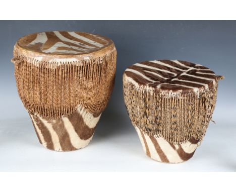 Two mid-20th century Kenyan drums, strung with zebra hide to top and sides, heights 39cm and 29cm.Buyer’s Premium 29.4% (incl