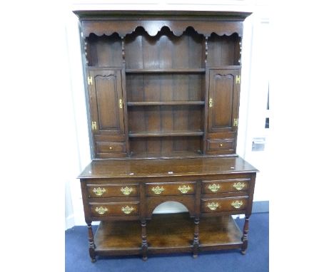 AN OAK DRESSER, the plate rack with twin cupboards and single drawers, the base with five various drawers on turned front sup