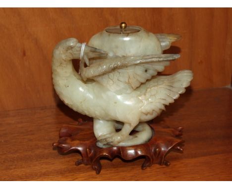 A jade-type hardstone model of a bird supporting a beaten white metal lidded stone pot between its wings, on carved wood stan