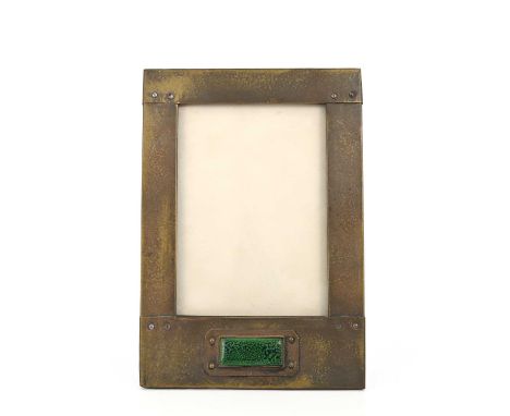 An Arts and Crafts brass and enamelled plaque photo frame, rectangular form with planished and riveted panels, set with green