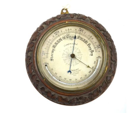A Victorian aneroid barometer with 20 cm silvered dial and curved mercury thermometer, brass bezel and ivy-carved oak frame, 