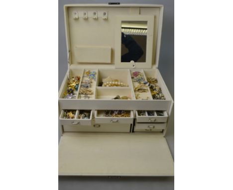 A cream multi-sectioned jewel box containing a quantity of fashion and costume jewellery including brooches, necklaces, cuffl