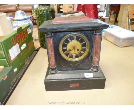 An old marble mantle clock with cream and black face, Roman numerals and marble pillars either side of the face, with scrolli