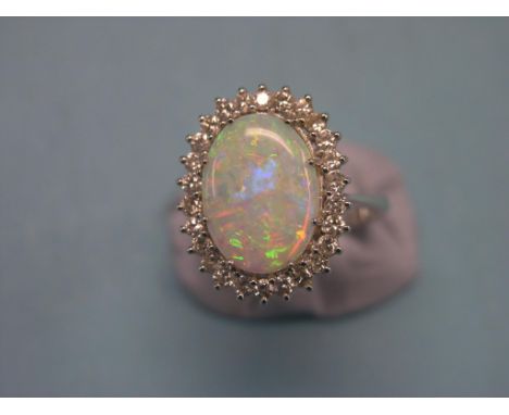 A large opal and diamond dress ring, central oval opal and numerous surrounding diamond chips, raised claw setting, white met