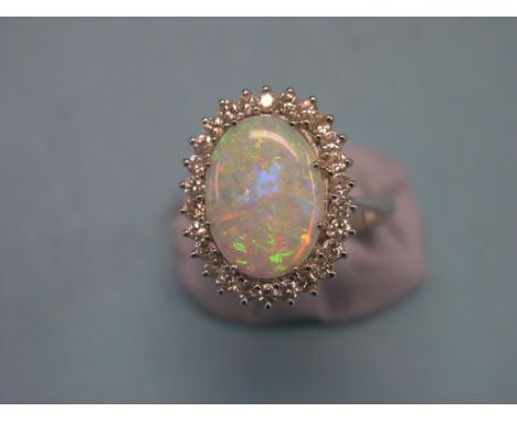 A large opal and diamond dress ring, central oval opal and numerous surrounding diamond chips, raised claw setting, white met