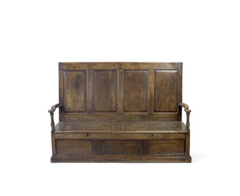 A mid-18th century oak box settleThe back with four fielded panels, the out swept arms with baluster supports, the seat with 