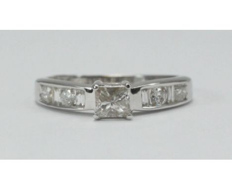 An 18ct white gold solitaire diamond ring, corner set with a princess-cut diamond and channel set with two baguette and two r