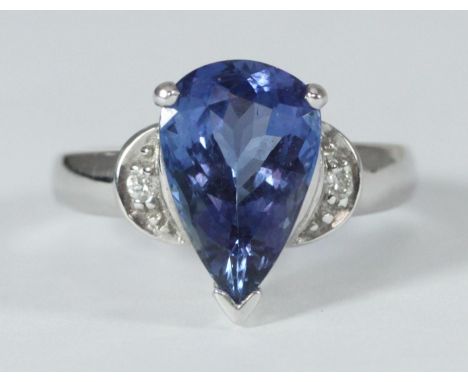 An 18ct white gold ring set with a pear shaped tanzanite, with a round brilliant-cut diamond to each shoulder.  The tanzanite