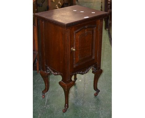 A Thomas Edward & Sons oak bedside cabinet, fielded panel door, foliate apron, ceramic castor