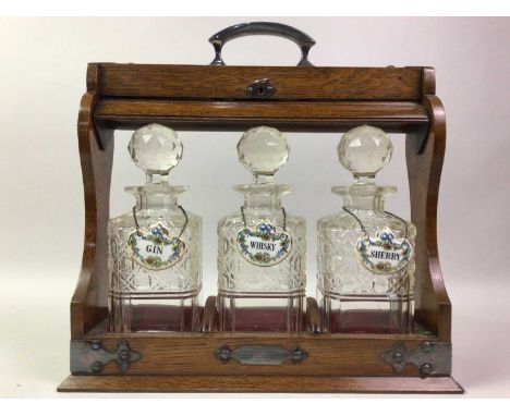 EDWARDIAN OAK TANTALUS, EARLY 20TH CENTURY  fitted with three square formed cut glass decanters with stoppers, with silver pl