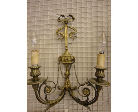 A SET OF THREE BRASS TWO LIGHT WALL SCONCES IN THE NEO-CLASSICAL TASTE, suspended from a tied ribbon, decorated with ram's he