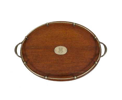 AN EDWARDIAN BRASS MOUNTED STAINED OAK OVAL SERVING TRAY with raised gallery rail and twin handles, with button feet stamped 
