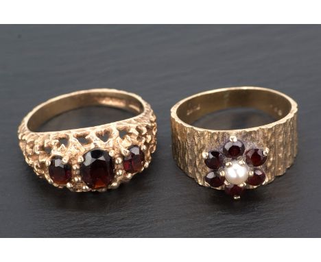  Two 9ct yellow gold and garnet rings the first of pierced bark design, set with three oval cut garnets, ring size O, the sec
