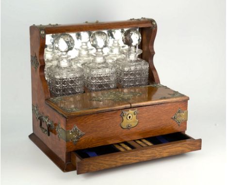  A Victorian oak cased three bottle tantalus with three matching cut glass decanters, bevelled mirror back plate, the case br
