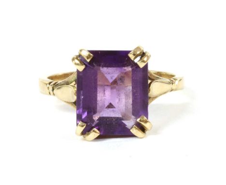 A gold single stone amethyst ring, with an emerald cut amethyst, four claw set to trifurcated shoulders and a plain shank, te