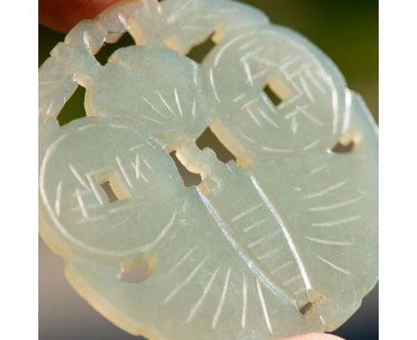 A hand carved and polished jade pendant, featuring carvings of two coins, a peach, and a fanned leaf. Dimensions: 2.25"L x 2.