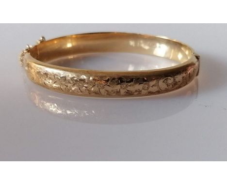A 9ct yellow gold hinged bangle with floral etched decoration and safety chain, hallmarked, 12.37g