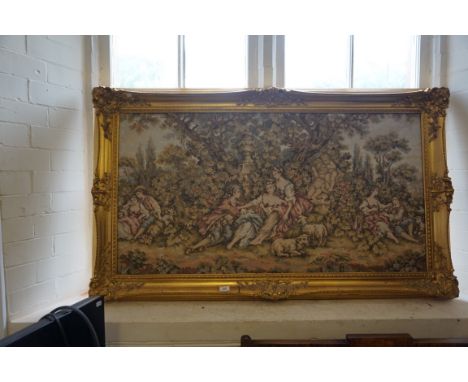 A large size tapestry panel depicting figures beside cherubs in landscape, inset in ornate gilt frame.