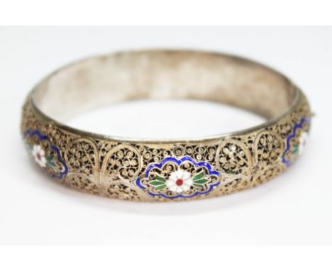 A white and gilt metal filigree bangle with enamel decoration, indistinctly marked, diam. approx. 58mm, gross wt. 25.93g.  Co
