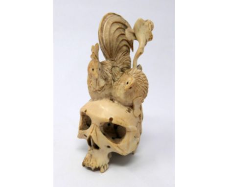 A late 19th century Japanese carved netsuke depicting a large skull topped with a rooster and chicken, H.8.4 W.4cm 