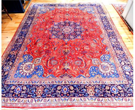 A large, fine, Isfahan carpet with a floral medallion on a red field, having blue spandrels, surrounded by one frieze and fou