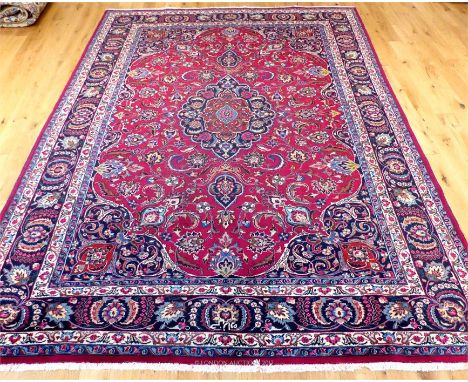 A signed Northeast Persian Mashad carpet, the central medallion on a deep red field, with midnight blue spandrels, surrounded