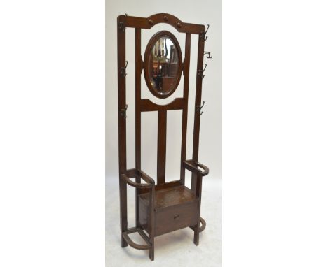 An early 20th century oak hall stand with central tilting oval framed mirror, brass coat hooks and twin apertures for sticks/