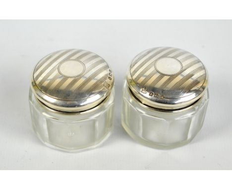 BOOTS PURE DRUG CO; a pair of George V hallmarked silver topped clear glass dressing table jars centred with vacant circular 
