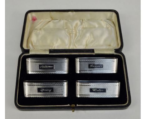 SANDERS & MACKENZIE; a cased set of four George V hallmarked silver engine turned decorated napkin rings of oblong form, each